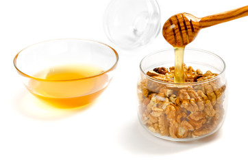 Jar with walnuts, a transparent saucer with honey on a white isolated background. Honey from a spoon flows into a jar of nuts. Close-up, a treat.