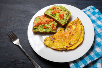 Healthy breakfast with omelette and guacamole toast on dark background