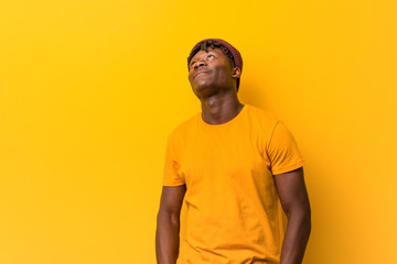 Young black man wearing rastas over yellow background dreaming of achieving goals and purposes