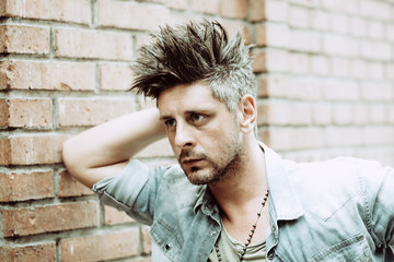 Portrait of handsome man leaning on brick wall, looking away to a side. Toned Image. Concept macho fashion city urban man.