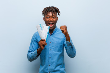 Young rasta black man holding an air tickets cheering carefree and excited. Victory concept.
