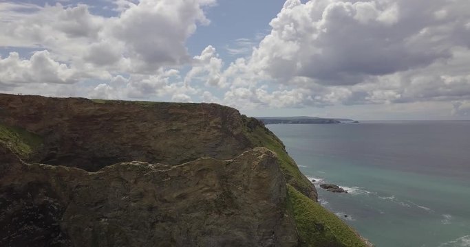 Drone view flying towards large cliffs off the coastline of cornwall looking out into the open ocean on a summers day