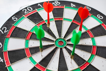 Green and red darts hitting in the dartboard in white background