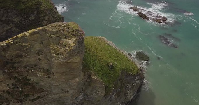 Drone aerial view of large cliff off the coastline of cornwall on a sunny day looking down at the ocean beneath