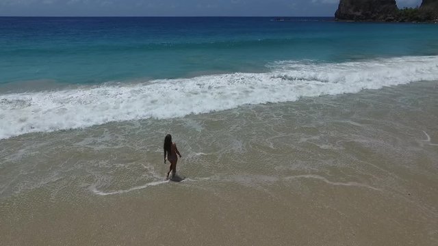 Girl in Bikini Walking Into Turquoise Ocean Water From Sandy Beach Aerial. Lailiang, Sumba Island Indonesia