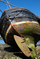 Old abandoned boat, showing the rusty propeller and rudder with peeling blue and red paint covered...