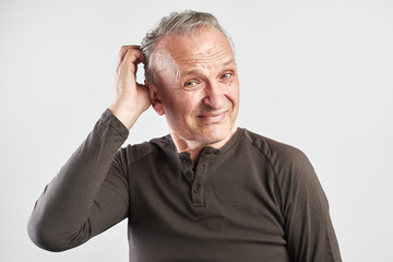 Stylish elderly middle-aged man scratches his head and thinking isolated in white studio, itching and discomfort of the scalp, dandruff