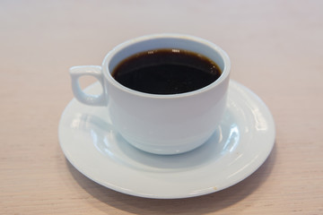 white cup, coffee in white sauce.Cup of hot coffee on table in cafe blur background . coffee beans in white porcelain cup decorated wild herbs .