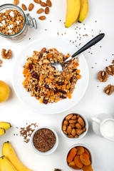 Granola muesli breakfast with with milk, dried apricots, cranberries, almonds and flax seeds in bowl on a white background. Healthy cereal breakfast.