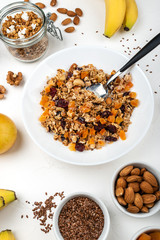 Granola muesli breakfast with with milk, dried apricots, cranberries, almonds and flax seeds in bowl on a white background. Healthy cereal breakfast.