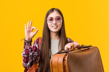 Young asian woman holding a suitcase cheerful and confident showing ok gesture.
