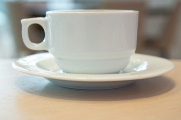 white cup, coffee in white sauce.Cup of hot coffee on table in cafe blur background . coffee beans in white porcelain cup decorated wild herbs .