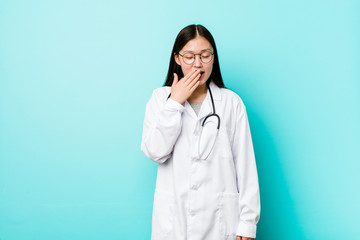 Young chinese doctor woman yawning showing a tired gesture covering mouth with hand.