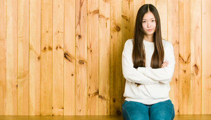 Fototapeta premium Young chinese woman sitting on a wooden place frowning face in displeasure, keeps arms folded.