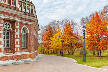 Autumn in Tsaritsyno Park in Moscow. Trees with bright colored leaves against facade of restored historical building on a cloudy autumn sky background