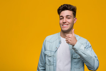 Young handsome student wearing a denim shirt smiling and raising thumb up