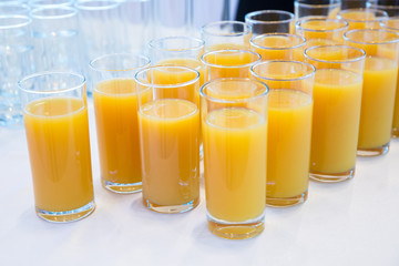 glasses of orange juice .Row of Glasses with Fresh Orange Juice. Catering concept. Bokeh blurred background. Selective focus . Group of glasses with juice on the table .