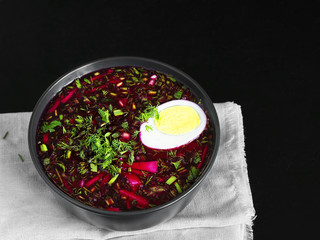 Cold beetroot soup in a black ceramic plate with half a boiled egg. The dish is located on a gray napkin on a black stone background. Healthy, natural food. Top view.