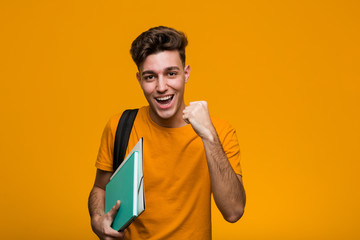 Young student man holding books celebrating a victory or success