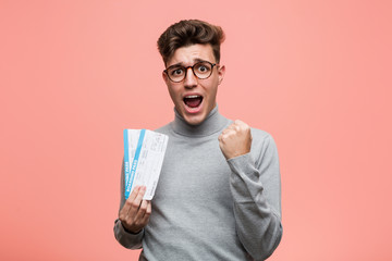 Young cool man holding an air tickets cheering carefree and excited. Victory concept.