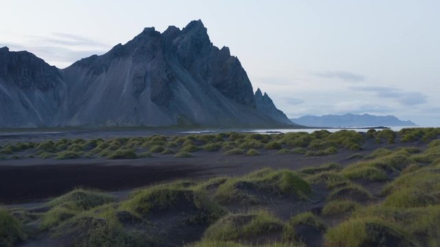 Aerial low shot of small dark dunes with grass in the Vestrahorn beach in Iceland.