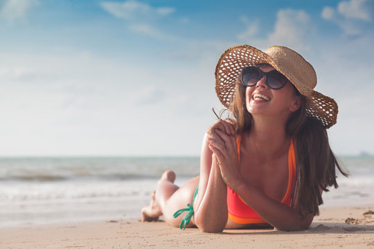 Beach woman funky happy and colorful wearing sunglasses and beach hat  having summer fun during travel holidays vacation. Young trendy cool hipster  woman in bikini lying in the sand. Stock Photo
