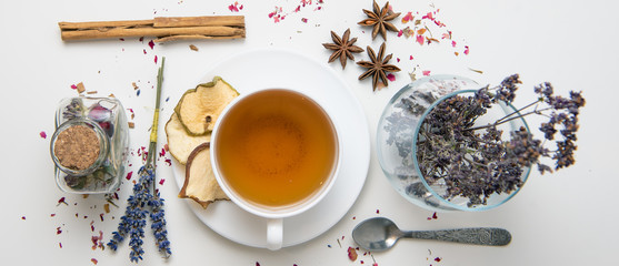 a white mug on a white table with herbal tea and herbal ingredients laid out on the table. Concept...