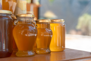 Jars of honey are on the table. Honey is in the lumen. Bokeh background is with sun light. Horizontal close-up. Space for text