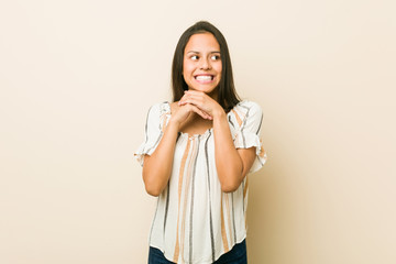 Young hispanic woman keeps hands under chin, is looking happily aside.