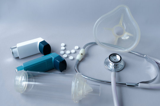 Treatment of asthma and lung conditions. Bronchodilator, anti-inflammatory, mask and inhalation chamber to control asthma due to allergies or colds on a gray background.