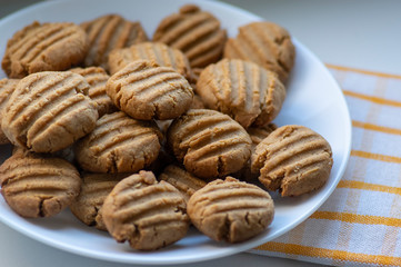 Pile of peanut butter biscuits on white plate, very tasty golden baked sweets, cookies served to eat