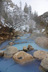 Fototapeta na wymiar VERTICAL: Gorgeous light blue spring water cascades from one pond to another