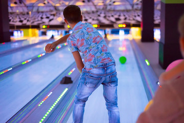 A boy throws balls at a bowling alley, knocking down pins.