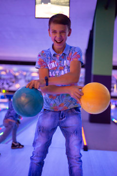 A boy holds bowling balls posing for the camera.