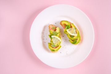 toasts with avocado salmon, basil leaves and a slice of lemon on a pink background. healthy breakfast concept.