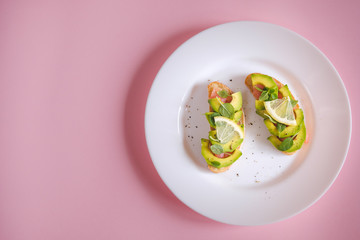 toasts with avocado salmon, basil leaves and a slice of lemon on a pink background. healthy breakfast concept.