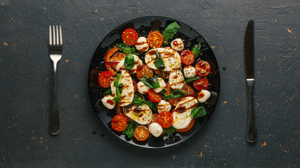 Italian caprese salad with chopped tomatoes, mozzarella cheese, basil, spices, balsamic vinegar and olive oil. Vegetarian dish. dark concrete background
