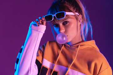Stylish pretty young 20s fashion teen girl model wear glasses blowing bubble gum looking at camera...