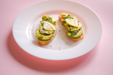 toasts with avocado salmon, basil leaves and a slice of lemon on a pink background. healthy breakfast concept.