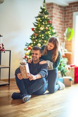 Obraz na płótnie Canvas Young beautiful couple smiling happy and confident. Woman surprise man with gift around christmas tree at home