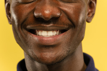 African-american young man's close up portrait on yellow studio background. Beautiful male model with well-kept skin. Concept of human emotions, facial expression, sales, ad. Looks calm and smiling.