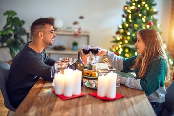 Young beautiful couple smiling happy and confident. Eating food and toasting with cup of wine celebrating christmas at home
