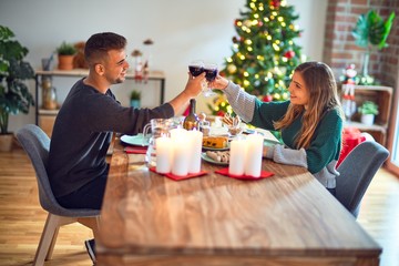Young beautiful couple smiling happy and confident. Eating food and toasting with cup of wine celebrating christmas at home