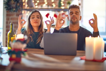 Young beautiful couple sitting using laptop around christmas decoration at home relax and smiling...