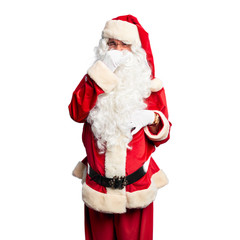 Middle age handsome man wearing Santa Claus costume and beard standing smelling something stinky and disgusting, intolerable smell, holding breath with fingers on nose. Bad smells concept.