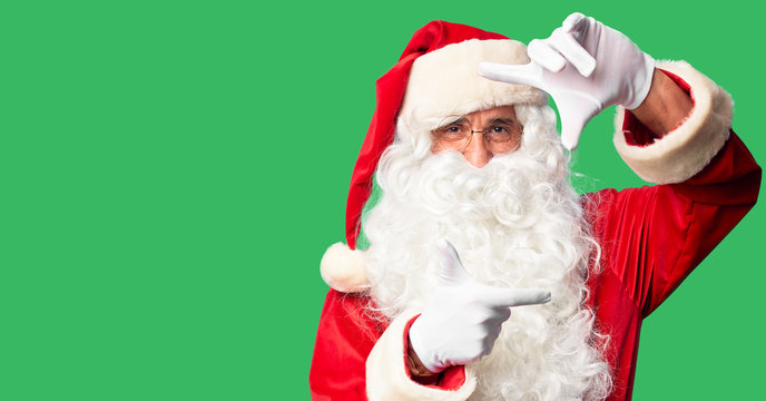 Middle age handsome man wearing Santa Claus costume and beard standing smiling making frame with hands and fingers with happy face. Creativity and photography concept.