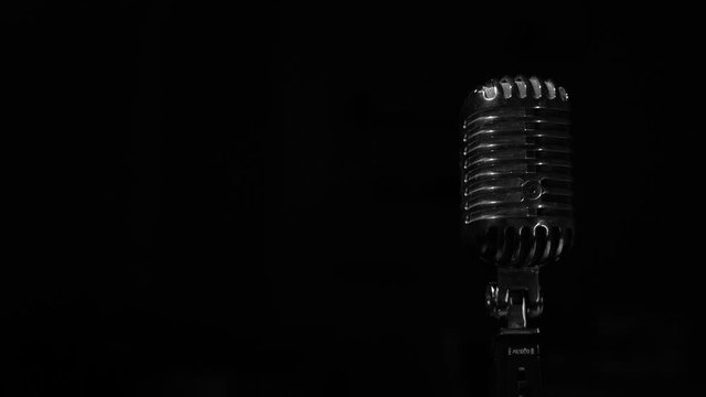Glare of white light flickers and shine on a chrome retro mic on right on black background. Professional vintage glare microphone for record or speak to audience on stage in dark empty club close up.