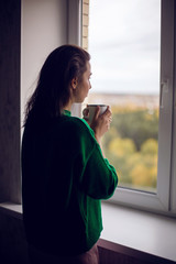 woman in a green sweater holds a metal mug of cocoa