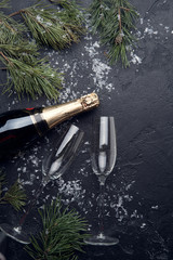 Image from above branches of spruce , bottle of champagne, two wine glasses on an empty black background.