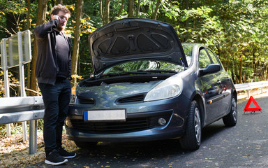 A broken car on the road, the driver holds an open hood and watches what has broken down, a...